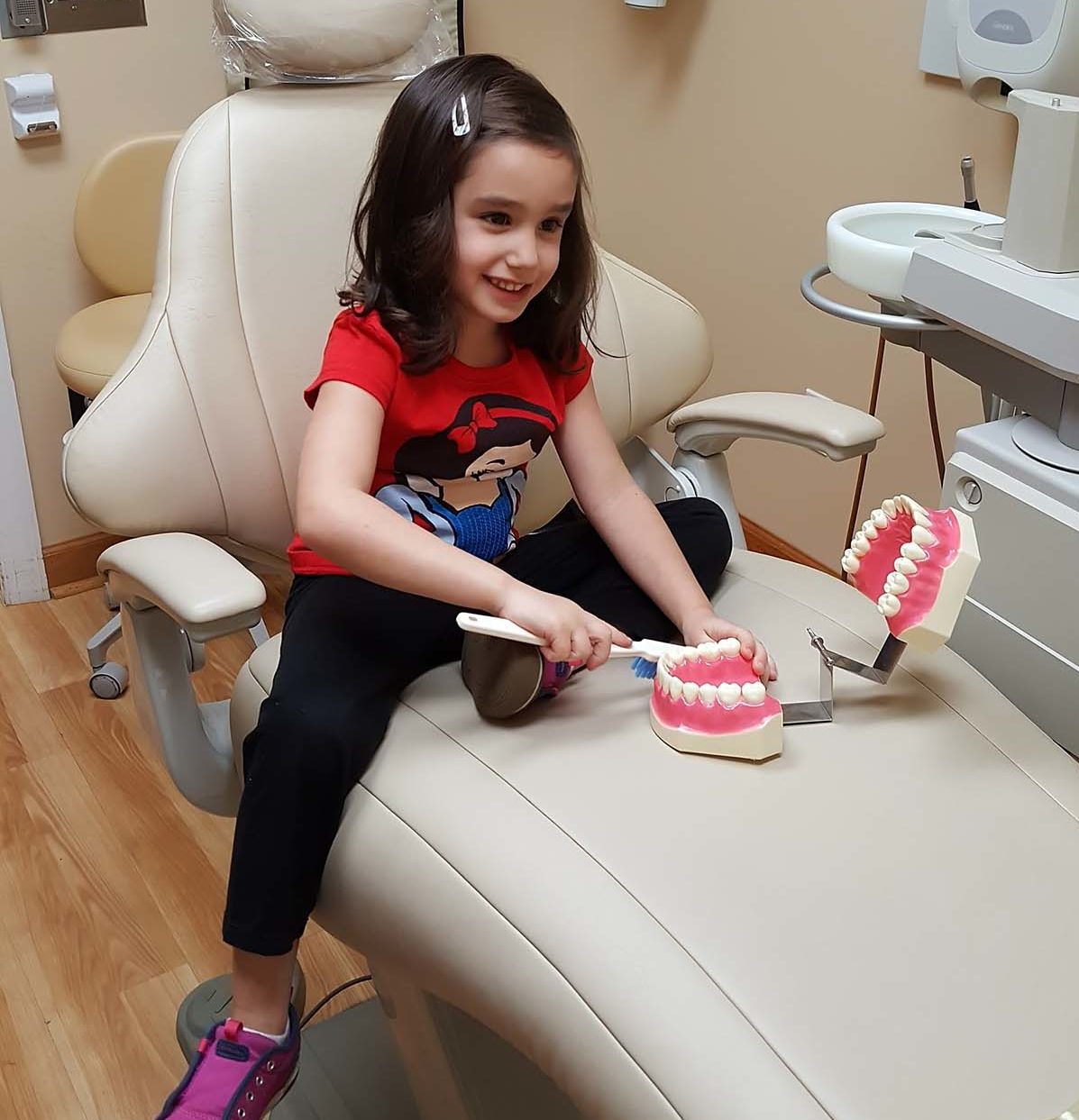 Little girl sitting on dentist chair with teeth model